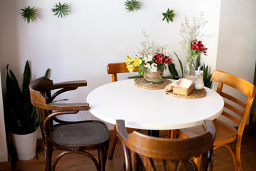 Modern and simple cafe interior with wooden classical furniture and flowers on white table.White decorative wall with greenery.