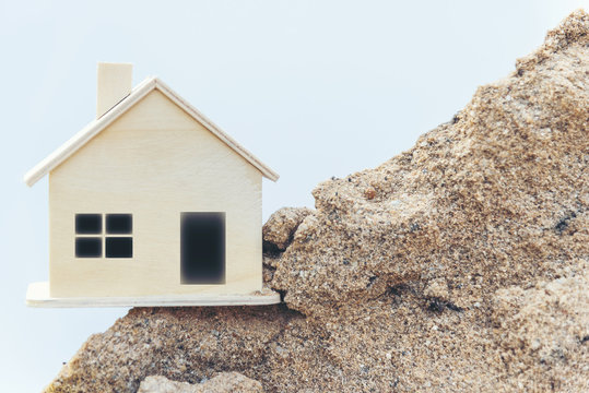Miniature replica wooden house is located on a sand pile.