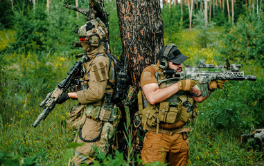 Airsoft men with guns stand back to back. Soldiers stand on hill and on call in the forest