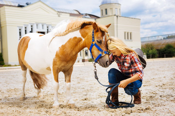 Happy meeting. Blonde-haired girl feeling extremely happy seeing pony after taking very long leave