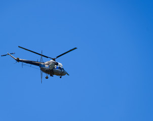 A helicopter of agricultural aviation is flying in the blue sky.