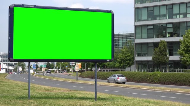 A billboard with a green screen by a road in an urban area