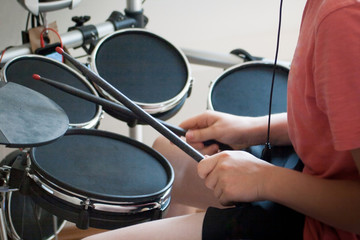 unrecognized boy in pink t-shirt practicing electronic drums with black drumsticks