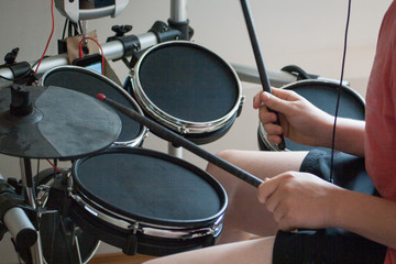 Fototapeta na wymiar unrecognized boy playing electronic drums with black drumsticks