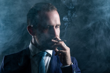 Fototapeta na wymiar Elegant Man with Beard Smoking a Cigarette Surrounded with Smoke