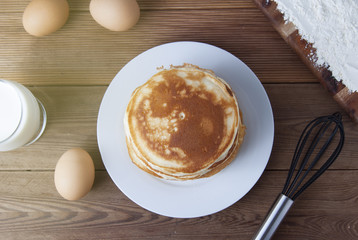 Cooking pancake on wooden background top view ingredients for making pancakes: milk, eggs, flour.
