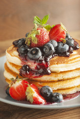 American pancakes served with strawberry and blueberry jam, delicious dessert for breakfast, rustic style, wooden background.