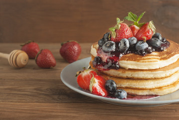 Homemade pancakes or fritters served with strawberry and blueberry jam, delicious dessert for breakfast, rustic style, wooden background. Copy space.