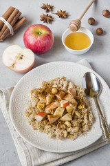 Oatmeal with fresh apples, nuts and cinnamon for Breakfast on the table, close-up, vertical