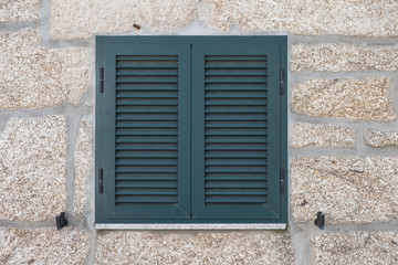 Ventana con contraventanas verdes en pared de piedra