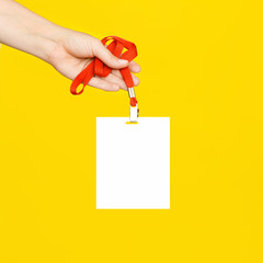 The woman's hand holds a clean white badge on a red cord on a bright yellow background.