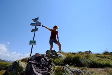 Donna indica la direzione del sentiero in cima ad una montagna, frecce direzionali presenti sulla scena