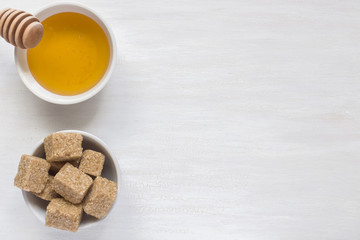 Brown sugar cane and honey in a plate on a light background. Copy space for text.