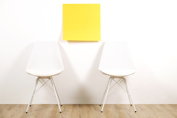 Pair of seats, two empty loft style chairs on wooden floor with blank ad poster & white wall background, yellow sticker, copy space for text. Interview invitation for vacant position concept. Close up