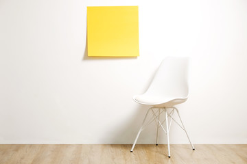 Single empty loft style chair on wooden floor with blank ad poster and white wall background, yellow sticker with copy space for your text. Interview invitation for vacant position concept. Close up.