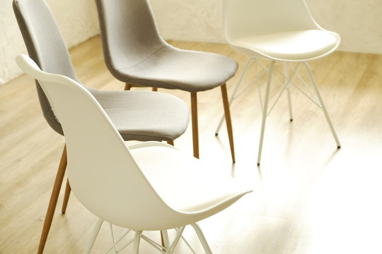Group therapy counseling for addicts & alcoholics concept. Multiple loft style empty chairs, white & gray, standing in row on wood textured floor. Four available seats. Copy space background, close up
