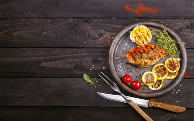 Obraz na płótnie Canvas Grilled chicken fillet with fresh thyme, cherry tomato, lemon, garlic and spices in a slate plate on black background