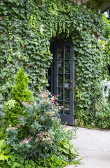 Vine covered building with flowers and wild roses and open french door - selective focus