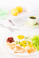 Scrambled eggs, fried bread, ketchup and lettuce leaves on a plate, cup of coffee and newspaper on the table.