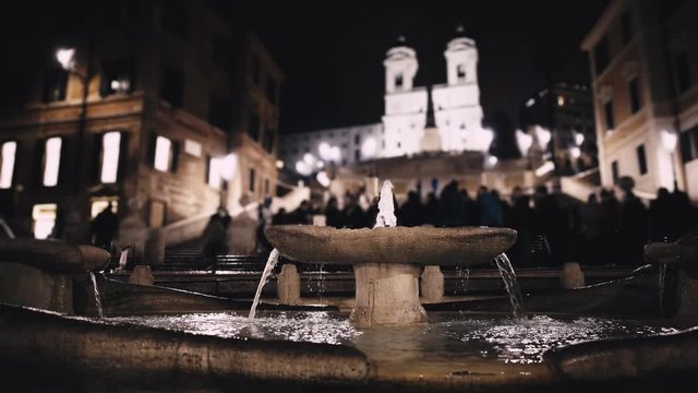 Fountain at Piazza di Spagna in Rome, Italy. A famous attraction on a cold winter night, February, 20 2018. Blurred people background. Locked down real time establishing shot