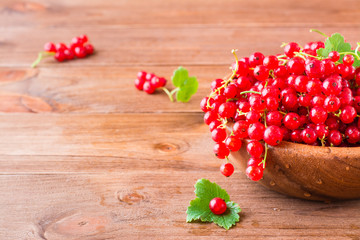 A bunch of fresh red currants in a wooden plate on a table. Copy space