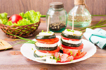 Original appetizer from fried zucchini, fresh tomatoes and feta cheese on a wooden skewer on a plate
