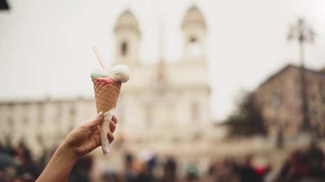 Hand of an unrecognizable young girl holding an ice cream cone over blurred Piazza di Spagna background. Rome, Italy. Winter. Locked down real time establishing shot