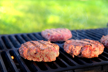 Three hamburger on the grill grid in the background of a green lawn