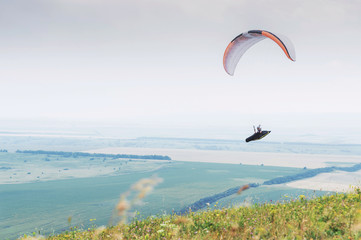 White orange paraglide with a paraglider in a cocoon against the background of fields of the sky and clouds. Paragliding Sports