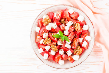 Fresh appetizer of tomatoes, feta cheese, walnuts, flax seeds and sesame seeds in a plate. Top view