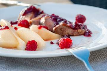 Grilled caramelized duck fillet with pieces of pear, raspberry and cowberry sauce on a plate with fork