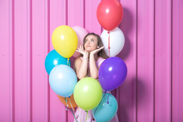 Fototapeta na wymiar Birthday girl with colored balloons against metal rose wall.