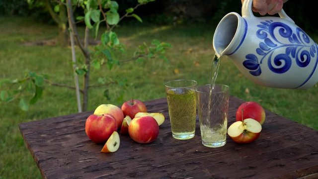 Traditional apple wine in the city of Frankfurt in Hesse. A jug of wine is on an old wooden table in the garden, around it are apples