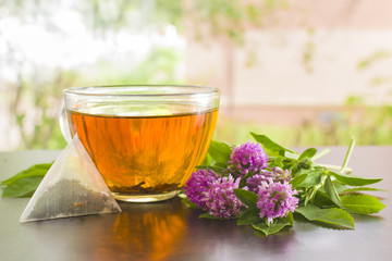 A transparent mug with tea on the table. Flowers of clover. Light background