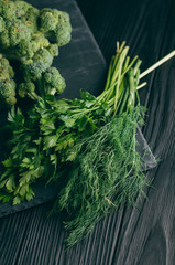 On a dark wooden table, fresh green broccoli, parsley, dill for your health. Flatlay. Recipe. Ingredients. Dietary food. Place under the text.