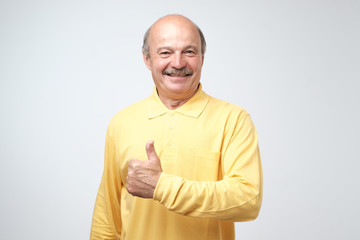 Handsome, bald man with his thumb up in sign of optimism on white background