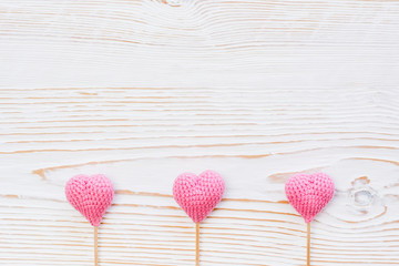 Three pink knitted hearts on sticks on a white wooden background