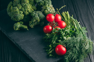 On a dark wooden table, fresh green broccoli, parsley, dill and cherry tomatoes for your health. Recipe. Ingredients. Dietary food. Place under the text. Top view.