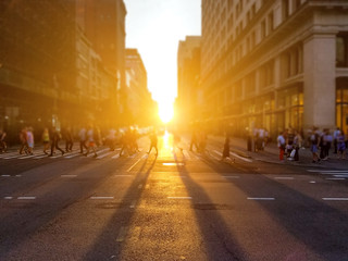 Group of anonymous people walk across the street on 5th Avenue in Manhattan New York City with sunlight setting in the background