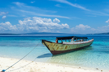 Fototapeta na wymiar An isolated small boat is staying at the beach surrounded by tortoise clear water of the ocean. The sky is in white clouds. No people. Indonesia, Sulawesi