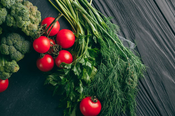 On a dark wooden table, fresh green broccoli, parsley, dill and cherry tomatoes for your health. Recipe. Ingredients. Dietary food. Place under the text. Top view.