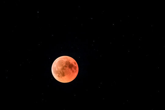 eclipsed red moon in a dark sky full of stars with planet mars