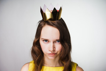 an evil young girl with blue eyes looks at the camera, in a yellow dress, a golden crown on her...