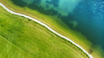 Aerial fly above the village road between the field and water