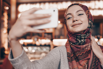 charming oriental girl with a beautiful headscarf smiling and making selfie on her smartphone