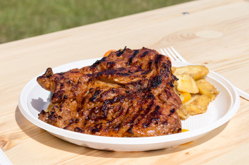 Street food with grilled pork neck on plastic plate.