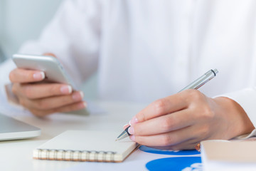 Businesswoman hand  working with multiple devices using smartphone and writing down on blank paper sheet at the office, Thinking and pay attention and curious situation. Business and finance concepts.