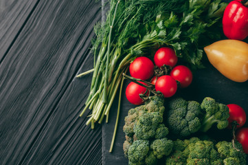 Fresh vegetables: cherry tomatoes, broccoli, pepper, dill, parsley on a dark wooden table. Recipe. Ingredients. Dietary food. Place under the text. View from above.