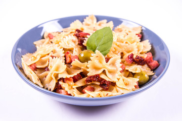 Farfalle pasta with sun dried tomato, ham and olives decorated with fresh mint