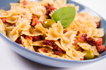 Farfalle pasta with sun dried tomato, ham and olives decorated with fresh mint